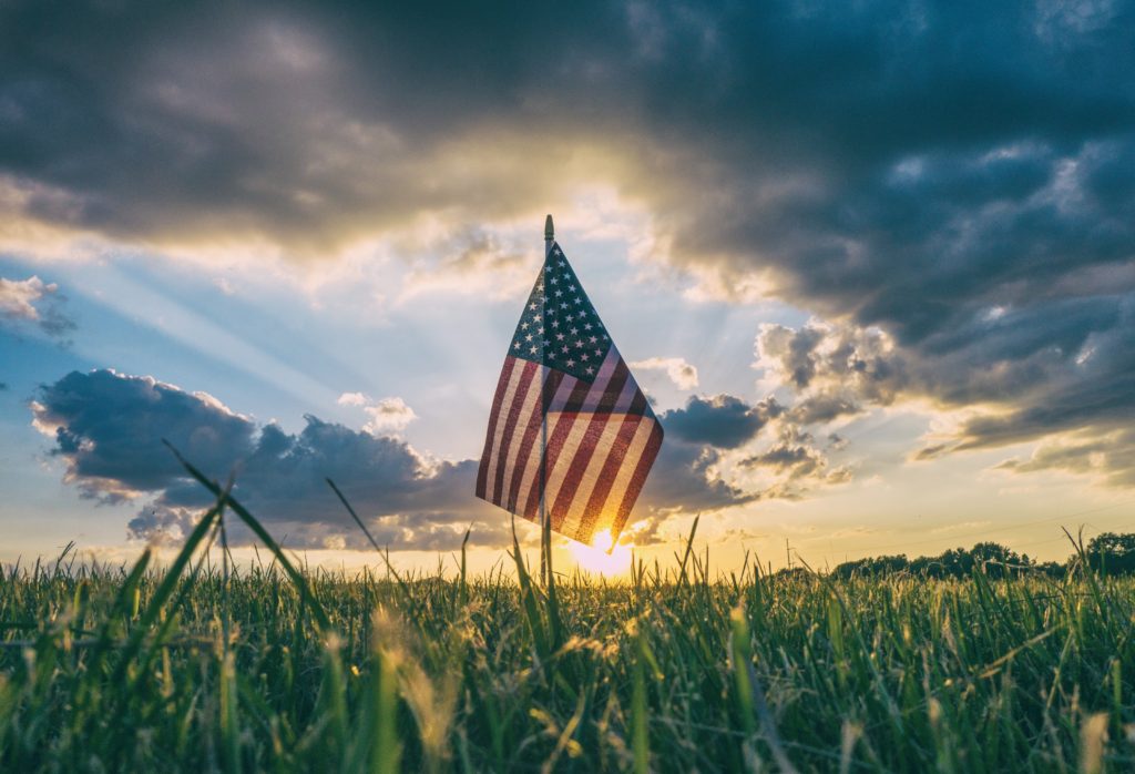 American flag on a grassy field with a cloudy sky