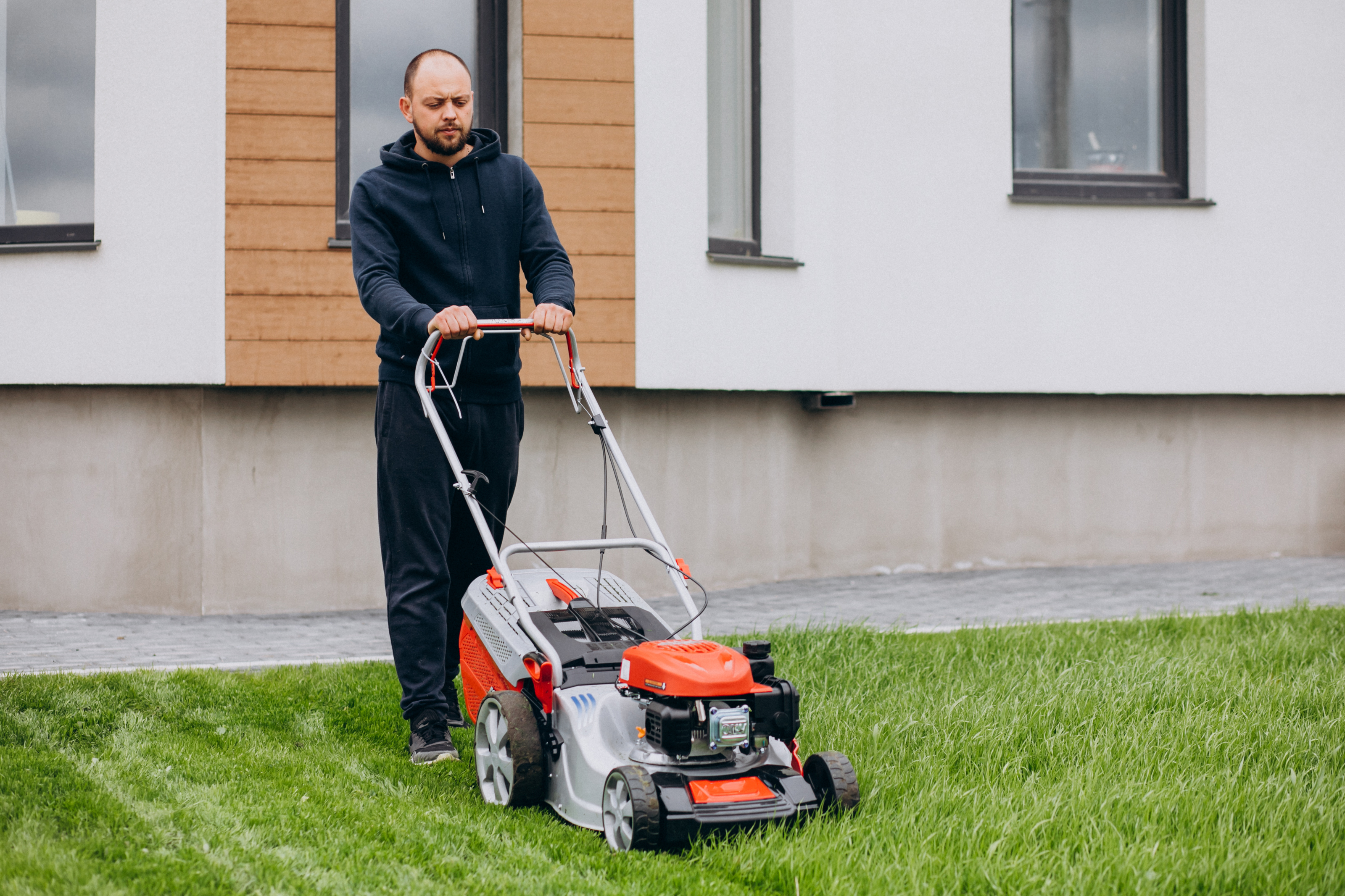 Man mowing the lawn with a red and silver lawnmower.