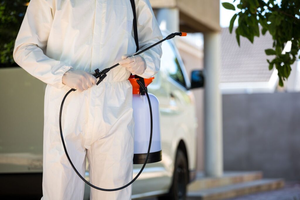A man in a white suit spraying, providing pest control and defense with seasonal pest control methods